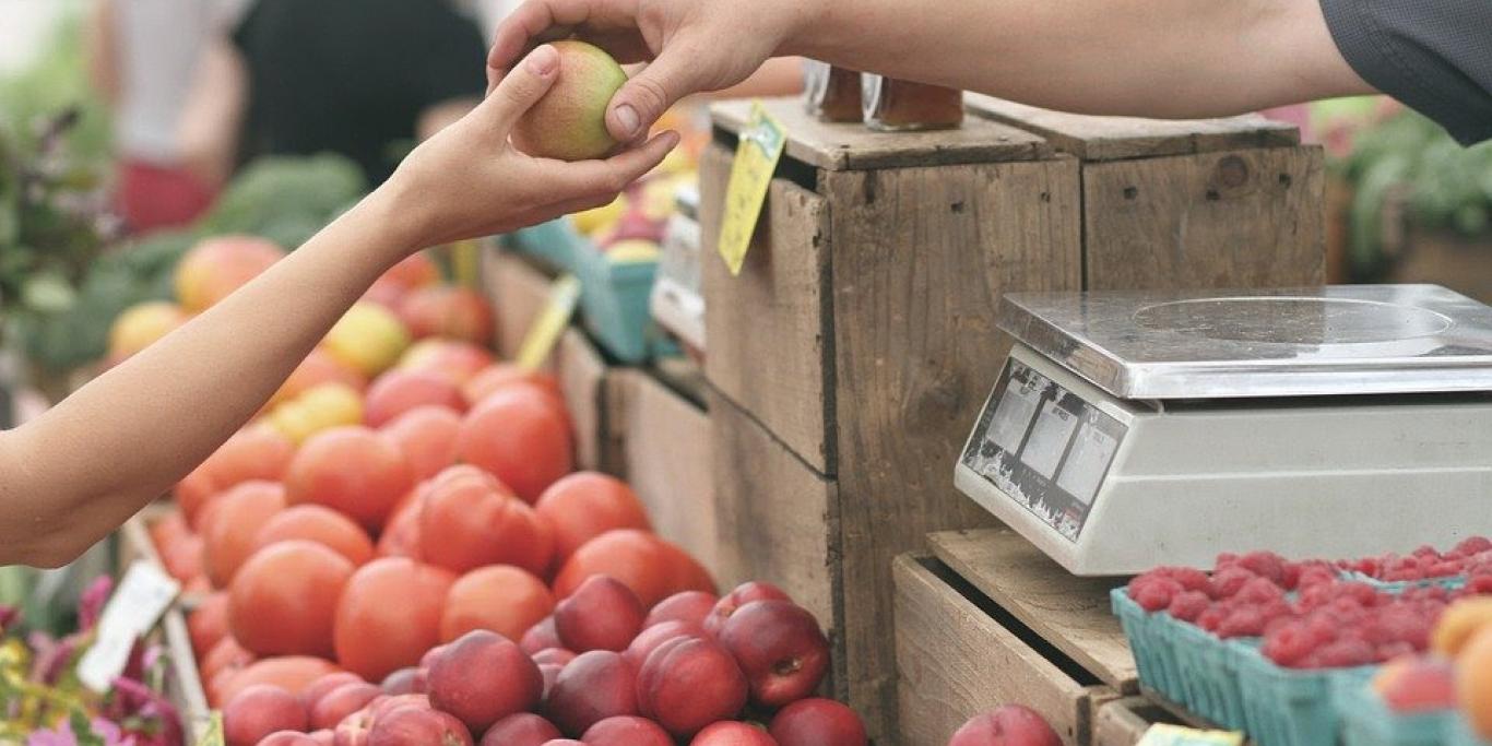 Photo of a farmers market vendor handing an apple to a customer